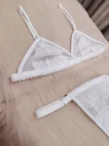 Conjunto de lencería compuesto por un corpiño triangular de microtul transparente con detalles de encaje floral en las copas y una tanga regulable con elástico ancho.