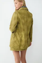 Chaqueta de manga larga color verde oliva con efecto gamuza, corte recto, cuello clásico, cierre frontal de botones y dos grandes bolsillos de parche delanteros.