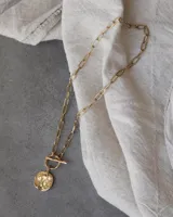 Collar de cadena de eslabones alargados con cierre frontal tipo T y dije circular de textura rústica e irregular.