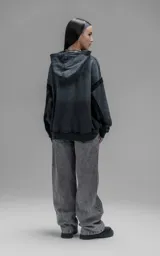 Hoodie oversize de corte crop en color gris oscuro con efecto desgastado. Presenta costuras expuestas, detalles de roturas en el ruedo y en la capucha, y bolsillos frontales con bordes reforzados.