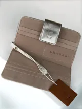 Billetera grande de cuero en color natural, con solapa externa en cuero metalizado dorado que presenta un logo grabado de un búho. El interior cuenta con múltiples ranuras para tarjetas y el nombre de la marca grabado.