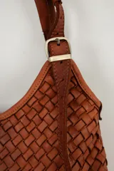 Cartera tipo hobo color suela, confeccionada en cuero con diseño trenzado y correa ajustable con hebilla metálica dorada.