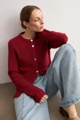 Chaqueta de punto en color bordó, con cuello redondo, manga larga y cierre frontal mediante botones metálicos. Presenta un diseño de tejido acanalado y corte recto.