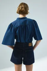 Blusa de denim de algodón suave, de color azul, con cuello mao, botonadura frontal y mangas cortas abullonadas.