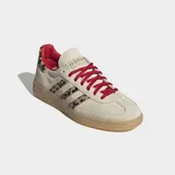Championes Adidas modelo Handball Spezial, con diseño clásico de perfil bajo. Presentan una base en tono beige con detalles de estampado animal print en las icónicas tres tiras laterales y en el talón. Incluyen cordones en color rojo vibrante, forro interior a tono y suela de caucho tipo goma.