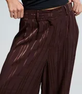 Pantalón de corte aladino confeccionado en viscosa y poliéster, con diseño de rayas verticales y acabado con leve transparencia. Presenta cintura alta, trabillas para cinturón y puños elásticos en el dobladillo.
