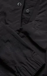 Chaqueta técnica liviana de microfibra con acabado mate, diseño con mangas desmontables que permiten convertirla en chaleco. Cuenta con cuello tipo camisa, cierre frontal oculto, cuatro bolsillos frontales de gran tamaño y puños elásticos. Incluye logo bordado en relieve en el pecho.