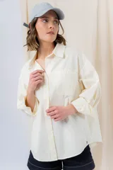 Camisa verde pastel de algodón, corte oversize, con cuello camisero, cierre con botones, mangas largas con puños con volados de encaje blanco, dos bolsillos frontales con solapa y ruedo irregular. 