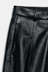 Pantalón de tiro alto con diseño de pierna ancha, confeccionado en tejido efecto piel. Cuenta con bolsillos delanteros, falsos bolsillos traseros de vivo y cierre frontal con cremallera y ganchos metálicos.
