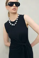 Vestido largo de punto color negro, sin mangas, con diseño entallado y un lazo lateral que permite ajustar la cintura.