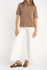 Sweater de tejido de punto fino en color arena, con cuello redondo y mangas cortas. Presenta un diseño minimalista con un pequeño detalle metálico en el ruedo.