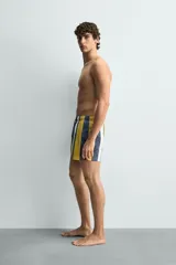 Bañador de hombre con estampado de rayas verticales anchas en tonos amarillo mostaza, azul oscuro desgastado, blanco y gris. Posee cintura elástica con cordón ajustable y bolsillos laterales.