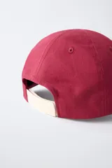 Gorra de béisbol azul marino con visera curva y detalle de borde en color crema. Presenta un bordado frontal con la palabra 'LONDON' en tipografía estilo varsity y texto adicional debajo.