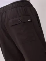 Bermuda de corte recto en color beige, confeccionada en una mezcla de algodón, lino y poliéster. Presenta cintura elástica con cordón ajustable, bolsillos laterales y una pequeña etiqueta decorativa en el ruedo.