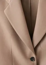 Chaqueta de traje color tostado con cuello de solapa, cierre frontal de dos botones, mangas largas y bolsillos de parche delanteros. Cuenta con forro interior y diseño recto.