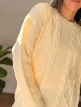Sweater de tejido de punto grueso color crema, con diseño de trenzas en relieve, cuello redondo, mangas largas y terminaciones acanaladas en puños, cuello y cintura.