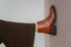 Bota corta de cuero marrón con panel trasero de gamuza en tono más oscuro, suela de goma negra y taco cuadrado bajo.