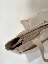 Cartera tipo tote de cuero graneado negro, con diseño clásico y textura uniforme. Cuenta con doble asa de hombro, bolsillo frontal con cierre magnético, bolsillo trasero con cierre metálico y compartimento principal con cierre. El interior está forrado y dispone de múltiples bolsillos organizadores.