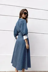 Vestido midi azul marino con rayas blancas, cuello solapa, escote en V y cierre frontal con botones. Cuenta con mangas abullonadas por debajo del codo con puños anchos a contraste, cinturón ajustable del mismo tejido con hebilla metálica y falda evasé.