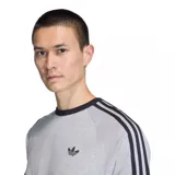 Remera de algodón gris con cuello y bordes de mangas en color negro. Presenta las icónicas tres tiras de Adidas en los hombros y el logo del trébol bordado en el pecho.