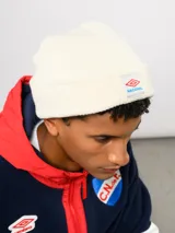 Gorro tipo beanie de tejido de punto color blanco crema, con parche frontal que incluye el logo de Umbro y la inscripción Nacional.