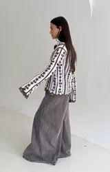 Camisa blanca de manga larga con delicados bordados florales verticales y detalles de encaje. Presenta cuello clásico, cierre frontal con botones y terminaciones festoneadas en los puños y el ruedo.