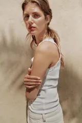 Musculosa de algodón color negro, con escote redondo y tiras anchas. Presenta detalles de encaje negro en los bordes y aplicación de perlas pequeñas alrededor del escote y los hombros.