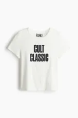 Remera de algodón color blanco con cuello redondo y mangas cortas. Presenta un estampado frontal con el texto 'CULT CLASSIC' en color negro y el logo de Charli XCX en la etiqueta interna del cuello.