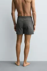 Bañador de hombre de largo medio, color celeste claro con rayas blancas horizontales. Presenta cintura elástica ajustable con cordón, bolsillos frontales y bolsillos traseros de plastrón. Incluye forro interior.