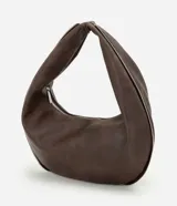Bolso tipo baguette de formato curvo, confeccionado en poliuretano con acabado que imita el cuero. Presenta una estructura flexible con asa integrada y cierre superior metálico aparente que recorre el contorno.