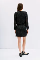 Vestido corto negro de manga larga con lentejuelas. Presenta escote redondo y un lazo ajustable en la cintura que frunce la falda. Las mangas son amplias y semitransparentes.