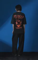 Remera de manga corta con cuello redondo y calce oversize, color negro con efecto nevado. Presenta una estampa frontal en color naranja con diseño gráfico de un rostro rodeado de llamas y texto tipográfico.