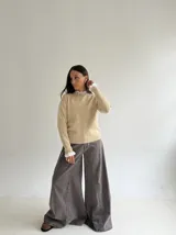 Sweater de punto color beige, con cuello redondo adornado con apliques de pedrería y detalle de puntilla blanca en el cuello y los puños.