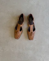 Mocasines color marrón claro, con detalle de borlas en la parte delantera y correa con hebilla dorada.