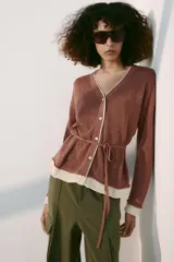 Chaqueta de punto color marrón con detalles en tono marfil en el escote en V, los puños y el ruedo. Cuenta con manga larga, cierre frontal con botones y un cinturón fino ajustable del mismo tejido.