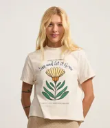 Remera color crema de algodón con cuello redondo y mangas cortas. Estampa frontal con una flor amarilla y texto en azul y verde.