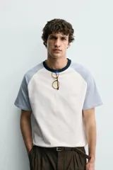 Camiseta de hombre regular fit, color blanco con mangas raglán cortas en azul claro y cuello redondo en rib azul marino.