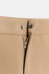Pantalón de tiro medio con pinzas delanteras, bolsillos laterales y falsos bolsillos de vivo en la parte trasera. Presenta un corte holgado que se estrecha hacia el tobillo, con bajo acabado en pliegues y cierre frontal con cremallera, botón interior y gancho.
