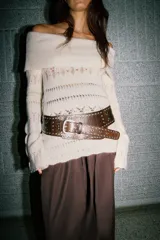 Jersey de punto color crema, con escote Bardot (hombros descubiertos) y manga larga acampanada. Presenta tejido calado con patrones horizontales y bajo festoneado.