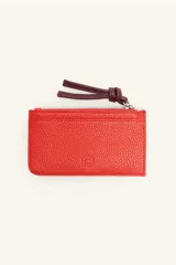 Monedero rectangular de cuero vacuno con textura granulada, color rojo. Cuenta con cierre superior metálico y un tirador de cuero en color bordó con detalle de nudo. Incluye un pequeño logo grabado en el centro.