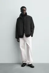 Sobrecamisa de corte relajado color beige, con cuello solapa en efecto piel de color negro. Presenta cierre frontal con cremallera, bolsillos de vivo en la cadera y mangas largas con puños ajustables.