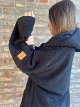 Campera de corderito negro con capucha y corte oversize. Presenta una etiqueta de cuero sintético con logo en la manga.