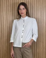 Camisa blanca de denim liviano y algodón, con cuello mao con volados, mangas tres cuartos con puños fruncidos y cierre frontal con botones tipo carey.