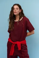 Blusa de lino color beige, de corte recto y mangas cortas, con costuras decorativas pespunteadas en tono rojizo que forman líneas verticales y horizontales.