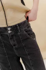 Pantalón de jean gris oscuro, estilo sastrero de tiro medio bajo y corte ancho (wide leg). Presenta costuras marcadas en el frente y un cinturón trenzado marrón con hebilla metálica.