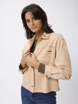 Campera tipo camisa de gamuza sintética en color beige, con cuello clásico, cierre frontal con botones metálicos y bolsillos frontales con solapa.
