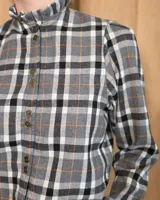 Camisa de algodón con estampado de rayas verticales finas, cuello alto con volados, cierre frontal con botones dobles y mangas largas con puños elásticos terminados en volados.