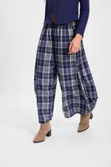 Pantalón de corte holgado con silueta tipo balloon, confeccionado en tela a cuadros. Presenta cintura elástica con cordón ajustable y cortes laterales circulares que aportan volumen a la prenda.