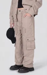 Pantalón cargo de corte oversize y silueta estructurada, color beige. Confeccionado en microfibra pesada, cuenta con cintura elástica con cordón de ajuste, cierre frontal con botón, bolsillos laterales y bolsillos cargo de gran tamaño con tapa y broches a presión.