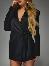 Vestido tipo blazer negro de corte entallado, con solapas clásicas, mangas largas y cierre frontal cruzado con lazo ajustable en la cintura.